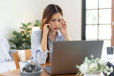 Kadın serbest çalışan, dizüstü bilgisayarda iş raporlarını okurken ve merkez ofisteki oturma odasındaki masada çalışırken strateji planını düşünmekten dolayı stresli ve baş ağrısı çekiyor..