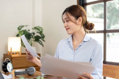 İşletme verilerini ve finansal grafiklerini okuyan serbest çalışan bir kadın, merkez ofisin oturma odasındaki masada dizüstü bilgisayarla çalışıyor..