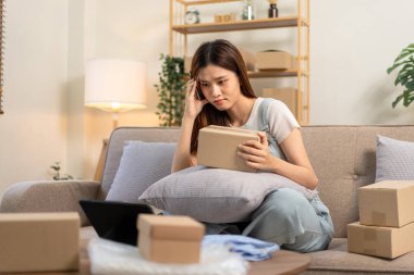 Genç girişimci, online siparişleri ve tabletteki müşteri verilerini kontrol ederken kanepede rahat otururken ve merkez ofisteki oturma odasında çalışırken kendini stresli hissediyor..