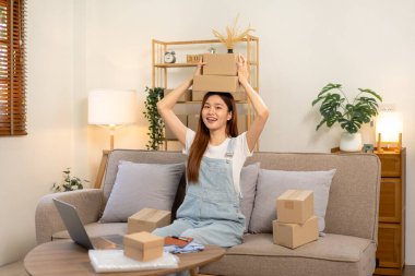 Genç girişimci karton kutuları elinde tutuyor ve satıştaki başarısından sonra koltukta rahat bir şekilde otururken ve ana ofisteki oturma odasında çalışırken kafasının üzerine yerleştiriyor..