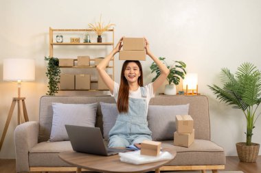 Genç girişimci karton kutuları elinde tutuyor ve satıştaki başarısından sonra koltukta rahat bir şekilde otururken ve ana ofisteki oturma odasında çalışırken kafasının üzerine yerleştiriyor..