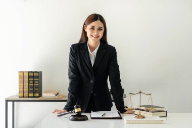 Avukatlık bürosundaki kameraya bakıp gülümserken pirinç pullar ve adalet çekiciyle hukuki alanda çalışan bir kadın..