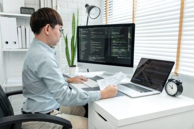 Male programmer is programing to developing program app and website of corporate while working to checking program code and debugging on multiple screen at modern software office.