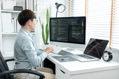Male programmer is programming to develop program app and website of corporate while working to checking program code and debugging on multiple screen at modern software office.