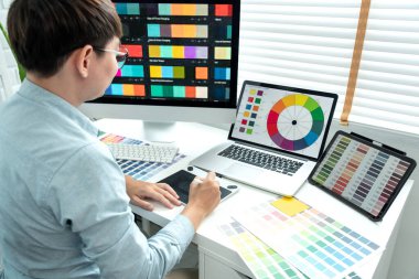 Erkek grafik tasarımcısı birçok ekrandan renk örnekleri seçiyor ve modern ofiste teknolojiyle çalışan grafik tasarımı için tablet dijital üzerinde çizim yapıyor..