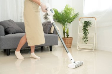 Temizlikçi, temizlik için elektrikli süpürge kullanıyor ve rutin ev temizliği yaparken oturma odasındaki kirleri temizliyor..