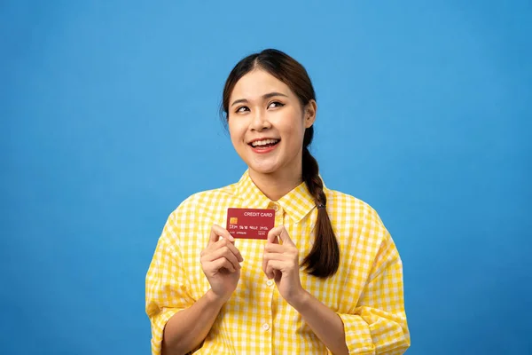 若いアジアの女性は新しいクレジットカードを示すために編組の髪型と笑顔であり ライトブルーの背景に隔離されたオンラインショッピングの準備を夢見ます — ストック写真