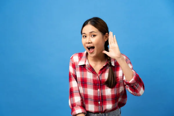 Young asian woman wearing gingham red shirt with braid hairstyle and excited face while use hand to listening secret story isolated over light blue background.
