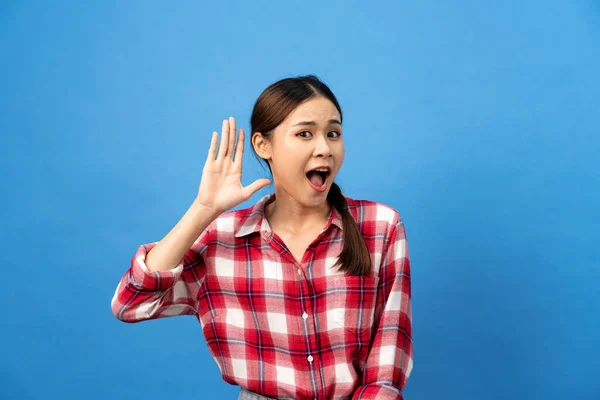 Young asian woman wearing gingham red shirt with braid hairstyle and excited face while use hand to listening secret story isolated over light blue background.