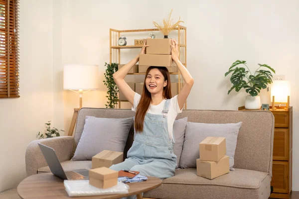 Genç girişimci karton kutuları elinde tutuyor ve satıştaki başarısından sonra koltukta rahat bir şekilde otururken ve ana ofisteki oturma odasında çalışırken kafasının üzerine yerleştiriyor..