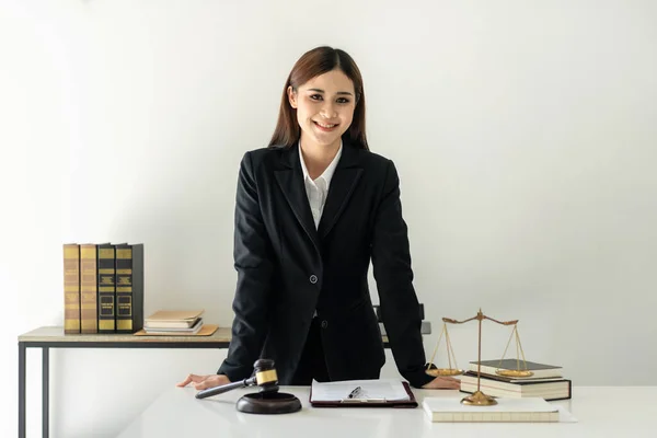 Business lawyer woman working the legal field on the table with brass scales and justice hammer while standing and smiling to looking at the camera in law firm office.