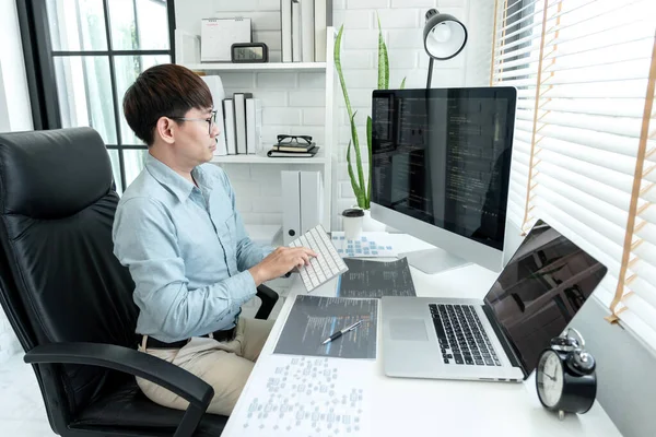 Male programmer is programming to develop program app and website of corporate while working to checking program code and debugging on multiple screen at modern software office.