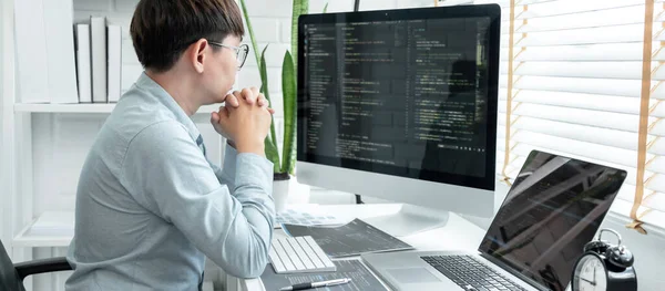 Male programmer is programing to developing program app and website of corporate while working to checking program code and debugging on multiple screen at modern software office.