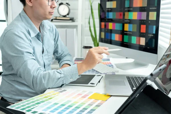 Male graphic designer is choosing color swatch samples on multiple screens and sketching on tablet digital to working graphic design with technology in modern office.