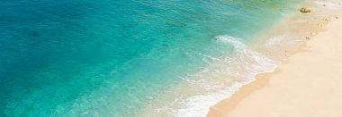 Panoramic photo of  beach with blue and green toned crystal clear sea and sand as a luxury summer holiday background or backdrop.