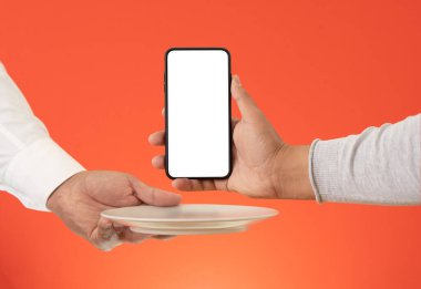 Hands holding empty serving plate and smartphone with screen mockup on isolated red background. Concept of food delivery and online meal order.
