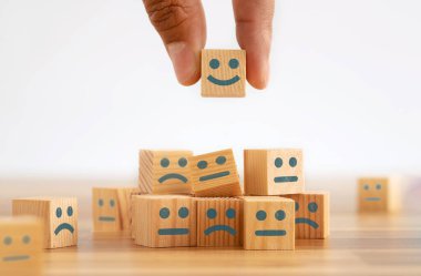 Hand picking smiling face wooden cube. Symbol of costumer service review. Concept of advantages and benefits of smiling face in business.