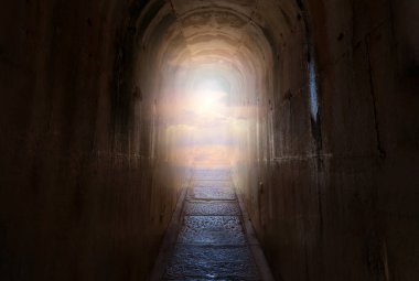 Dark tunnel with narrow path and end of the path shining sky and clouds. Heaven or paradise religion concept.