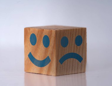 Photo of a wooden cube with happy and sad face expressions as a symbol of instat personality shifts. Concept of bipolar , unipolar and borderline.