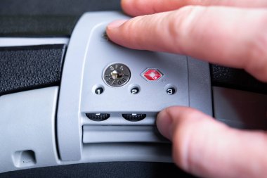 TSA 'yı (ABD Ulaştırma Güvenlik İdaresi) kilitleyen erkek parmaklar koyu bavulun kilidini kabul etti. Seyahat çantasındaki güvenlik kilidinin ayrıntıları..