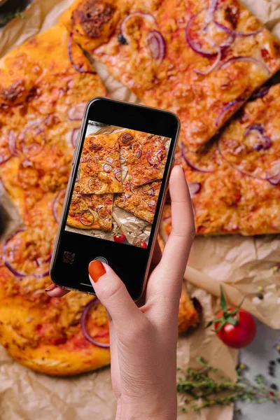 Female hand making a photo of pizza with a mobile phone