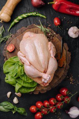 Whole raw chicken on a wooden board with spices for cooking, top view