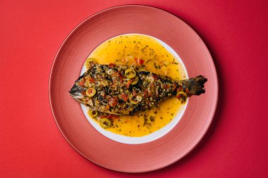 Dorado baked with special sauce on red plate