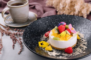 Round cheesecake with fruit decoration and cup of coffee