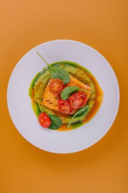 salmon steak with mashed avocado, decorated with basil leaves and cherry tomatoes