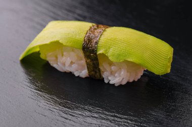 Siyah ahşap üzerinde avokado bulunan Japon suşisi.