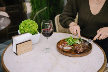 Kız terasta bir restoranda kızarmış biftek kesiyor.