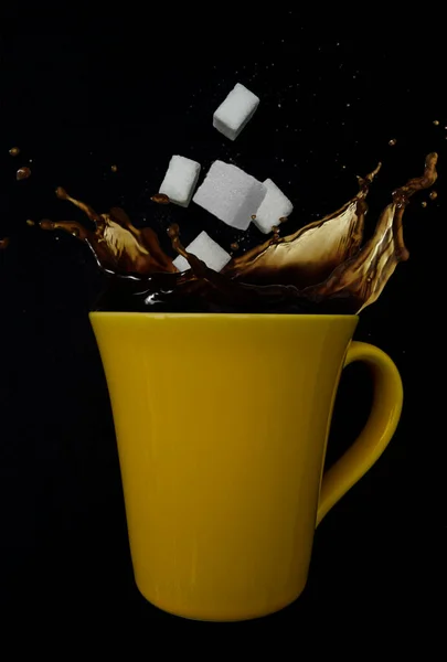 Yellow coffee cup with falling sugar lumps and splash motion with black background.