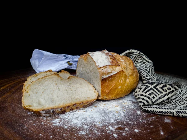 Sliced Italian bread wrapped in cloth with African illustration over wood and white flour with flour packet, black background and copy space.