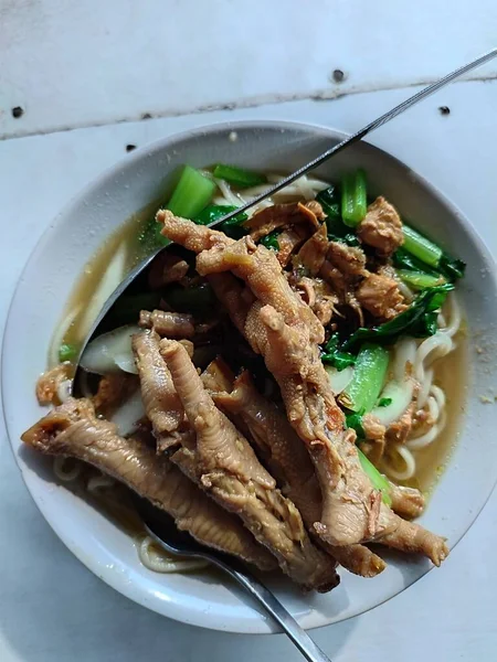 A Bowl of Chicken Noodles with Chicken Feet and mustard greens, Cheap and Delicious Street Food  from Indonesia