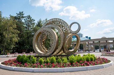 Abstract sculpture in the form of rings, made of polymeric materials, planted around a variety of plants and flowers