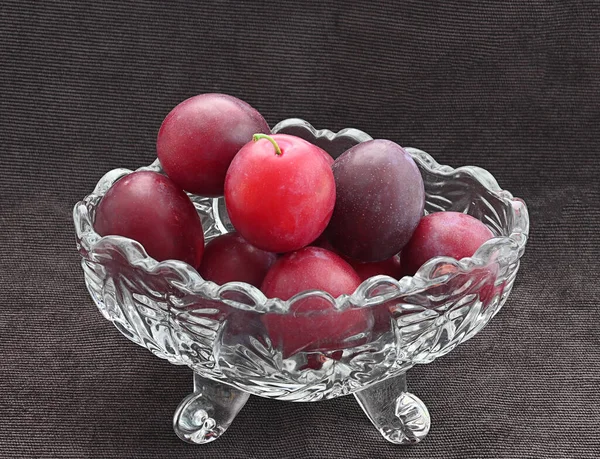 Ripe plum in a crystal bowl on a dark brown cloth background