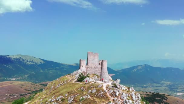 Letecký pohled na starobylý hrad na horském kopci, borový les na horském svahu. Bílé skály a křivolaká špinavá cesta podél hory. Horské pohoří v pozadí s modrou oblohou un léto slunečný den — Stock video