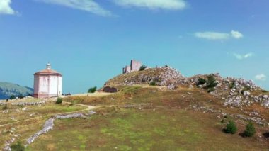 Dağ tepesindeki eski şatonun havadan görünüşü, dağ yamacındaki çam ormanı. Beyaz kayalar ve dağ boyunca kıvrımlı kirli yollar. Arka planda mavi gökyüzü olan dağ sıraları güneşli bir yaz günü