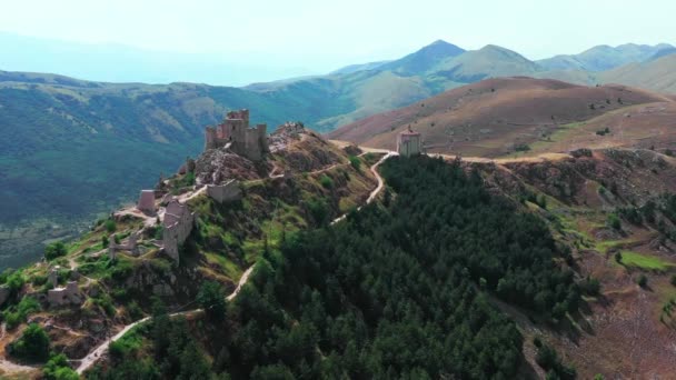 Вид на стародавній замок на гірському пагорбі, сосновий ліс на гірському схилі. Білі скелі і вигнута брудна дорога вздовж гори. Гірський хребет на задньому плані з блакитним небом влітку сонячний день — стокове відео