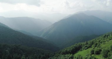 Ormanın üzerinde uçuyor. Yazın yeşil dağ ve yeşil orman, arka planda dağ sıraları, tepesinde bulutlar. yavaş çekim