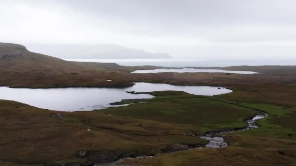Vista aérea de campos de campo con un río que va en el lago. Llanuras de las islas Feroe con campos, lago y río.Hermosa naturaleza salvaje del norte, Nubes en el cielo, niebla y cordillera en el fondo. — Vídeos de Stock