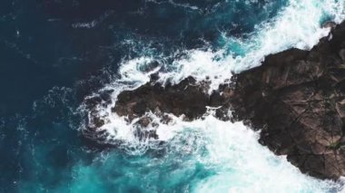 Dalgaların mavi okyanustaki kayalıklardaki havadan görüntüsü kopar. Yeşil doğa ve okyanusun insansız hava aracı görüntüsü..