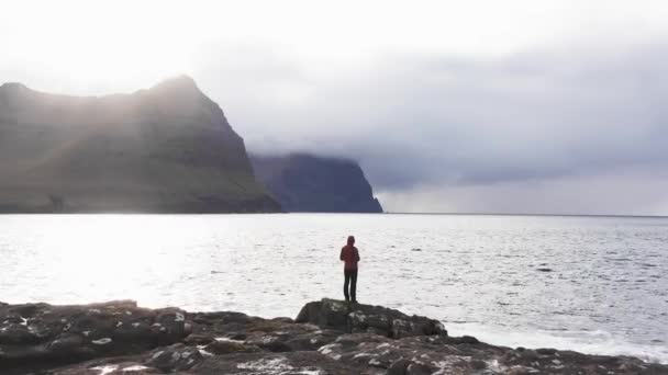 Vista aérea da mulher irreconhecível fica em penhasco de rocha olhando para o fundo da natureza selvagem das ilhas Faroe.Beleza natureza intocada, montanhas verde.Vídeo de mulher admirando ondas quebrar em penhascos rochas — Vídeo de Stock
