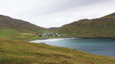 Denizin üzerinde uçan insansız hava aracı, yeşil çimlerle kaplı devasa ve görkemli bir uçurum çerçevesi. Güneşli bir yaz gününde uçurumun bodrumunda küçük bir köy.