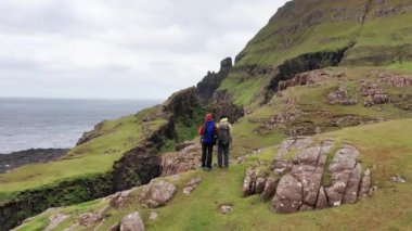 Faroe adalarındaki dev uçurumları, yeşil kayalık dağları, güçlü okyanus dalgalarını, bulutlu bir yaz gününde yeşil çayır ve vahşi doğada kayaları seyreden uçsuz bucaksız insanların hava manzarası..