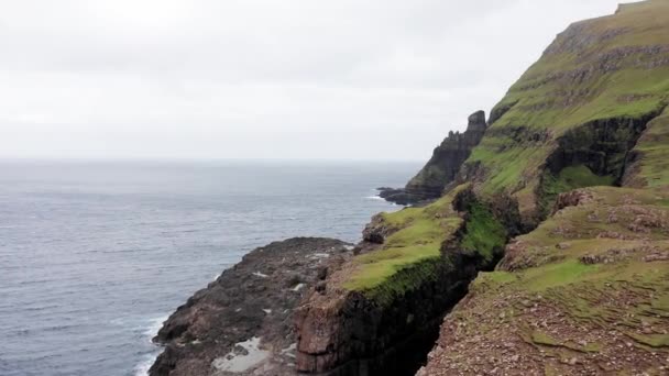 Luchtfoto van enorme kliffen in de Faeröer eilanden, groene rotsachtige berg, krachtige oceaangolven, in een bewolkte zomerdag, groene weide en rots in de wilde natuur, wild geen huis. — Stockvideo