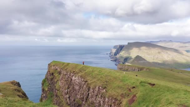 Légi visszapillantás hatalmas sziklák Feröer szigeteken, zöld sziklás hegy, erős óceán hullámok, egy felhős nyári napon, zöld rét és szikla a vad természetben, vad ház nélkül. — Stock videók