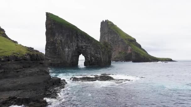 Vista aerea della pila di mare Rocky Drangarnir nelle Isole Faroe e la cascata skarosafossur Bella natura incontaminata, mare agitato, scogliere rocciose, onde creano schiuma marina, nuvole in cielo — Video Stock