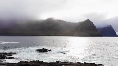 Saf doğanın havadan görünüşü. Kayalıklarda dalgaların görüntüsü bozuluyor. Kayalık kıyılarda okyanus dalgalarının kırılma görüntüsü, arka planda dağ sıraları. Dağın tepesindeki bulutlar.