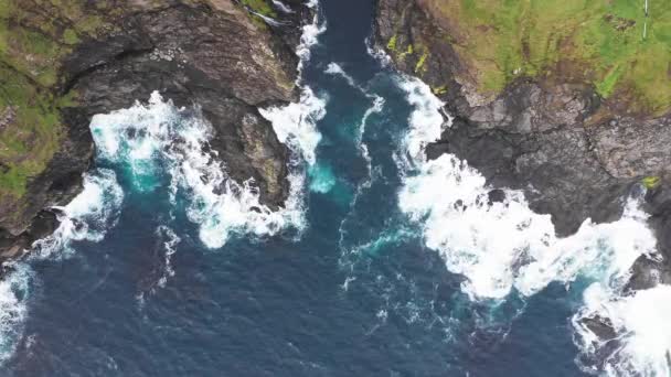 Vista aérea de las olas se rompen en las rocas de los acantilados de las Islas Feroe en un océano azul.Drone Imágenes aéreas de la naturaleza verde y el océano. — Vídeos de Stock